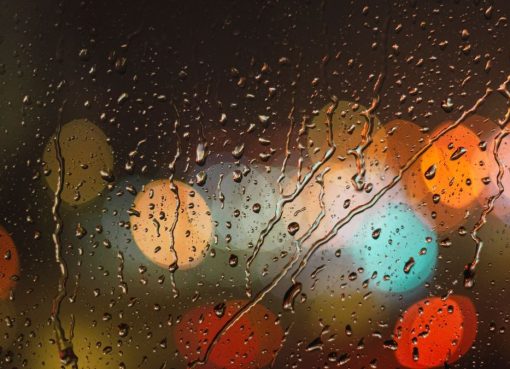 Close-up of raindrops on glass with blurred colorful city lights in the background.